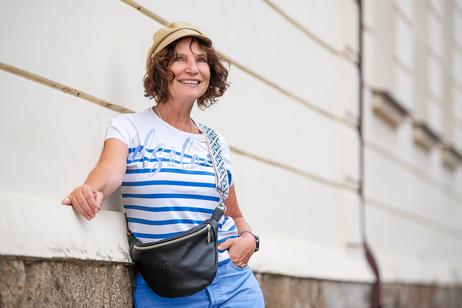 Woman in a striped shirt and cap standing outdoors with a car in the background