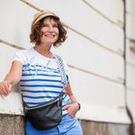 Woman in a striped shirt and cap standing outdoors with a car in the background