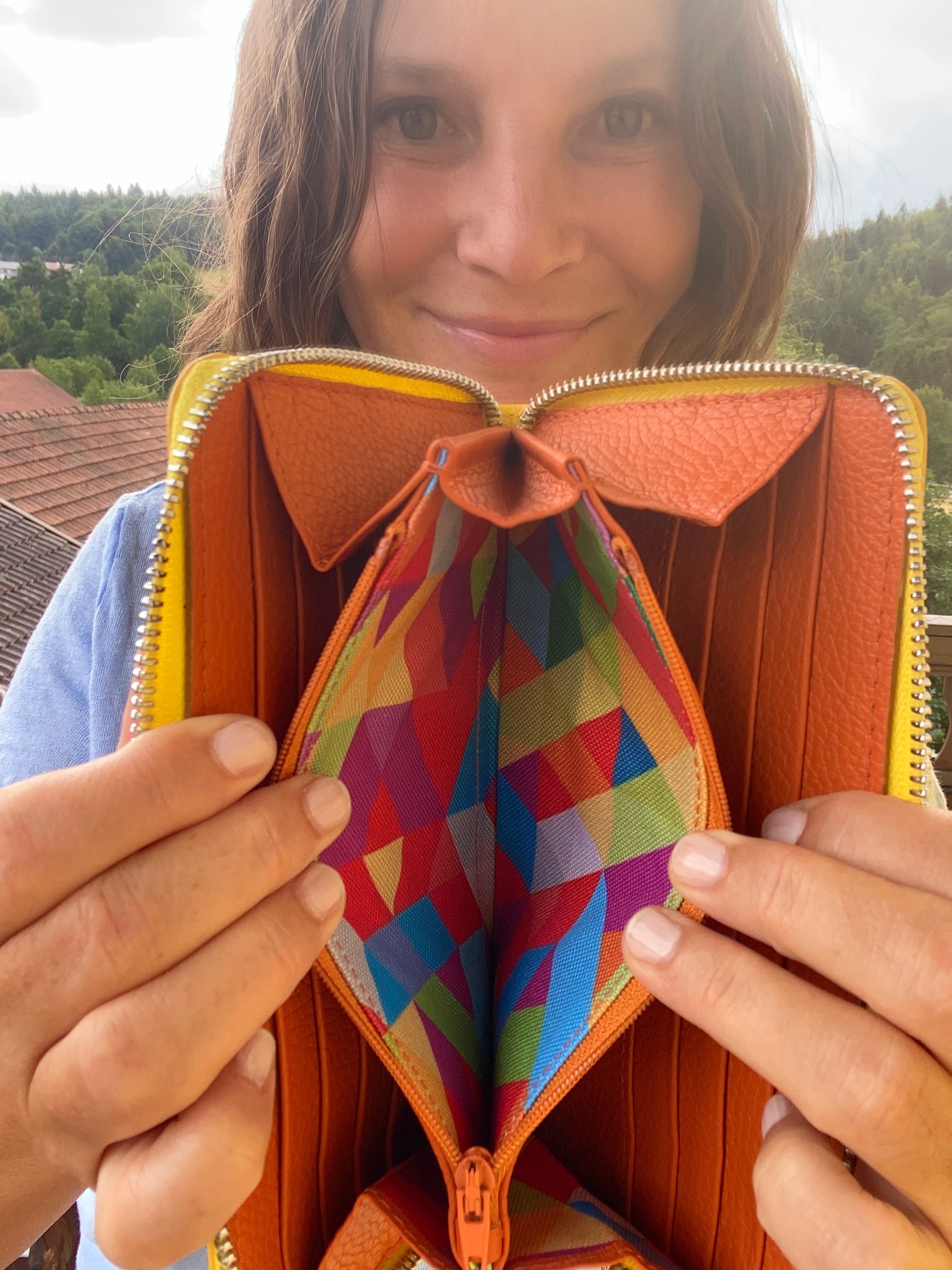 Person holding an open orange wallet with a colorful interior pocket.
