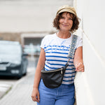 Woman in a striped shirt and cap standing outdoors with a car in the background