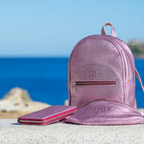 Pink backpack and wallet on a rock with ocean and sky background