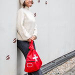 Person holding a red bag with a white cross against a light-colored wall.