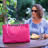 Woman sitting at a table outdoors with a pink bag and a cup of coffee.