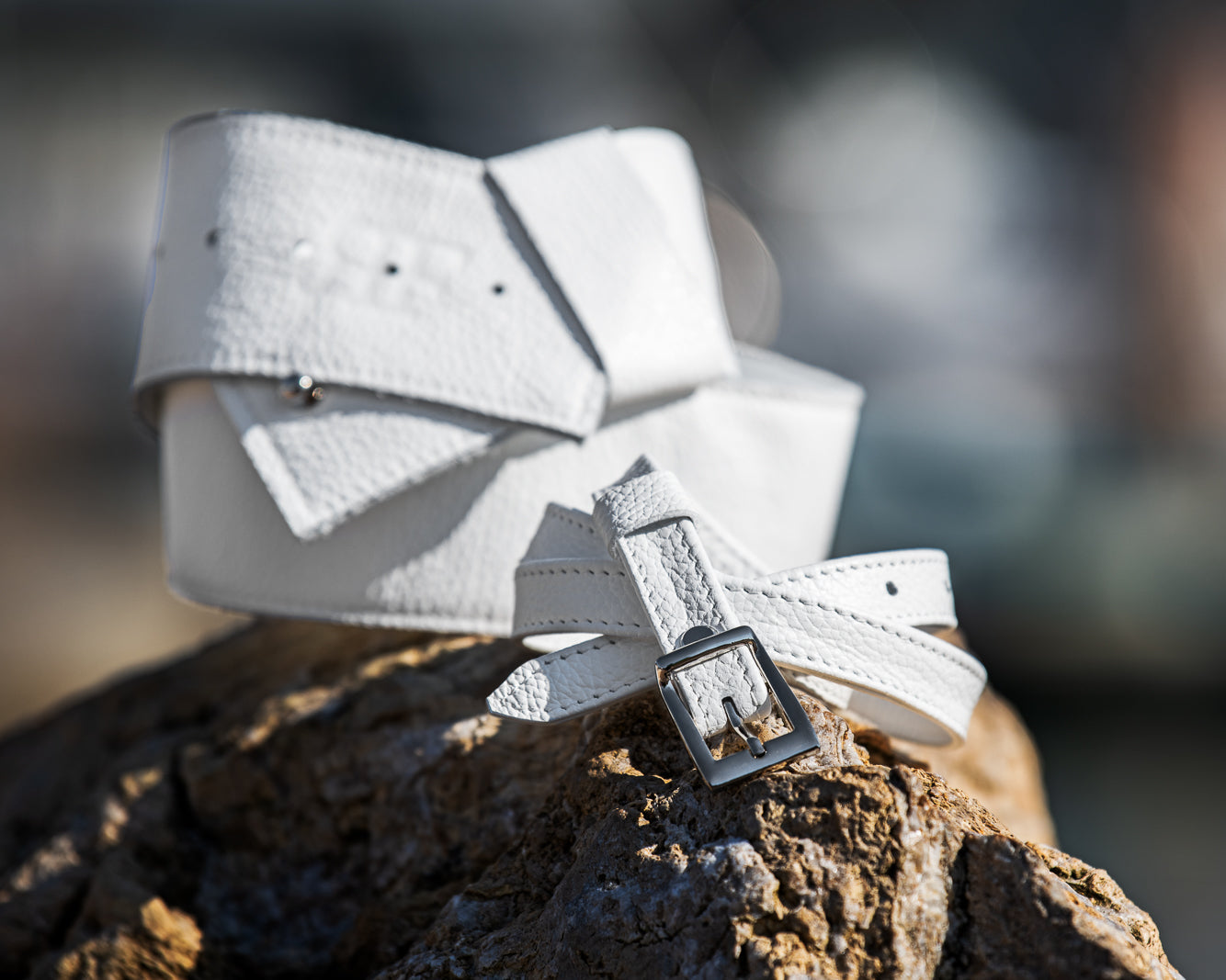 White leather belt with a silver buckle on a wooden surface