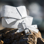 White leather belt with a silver buckle on a wooden surface