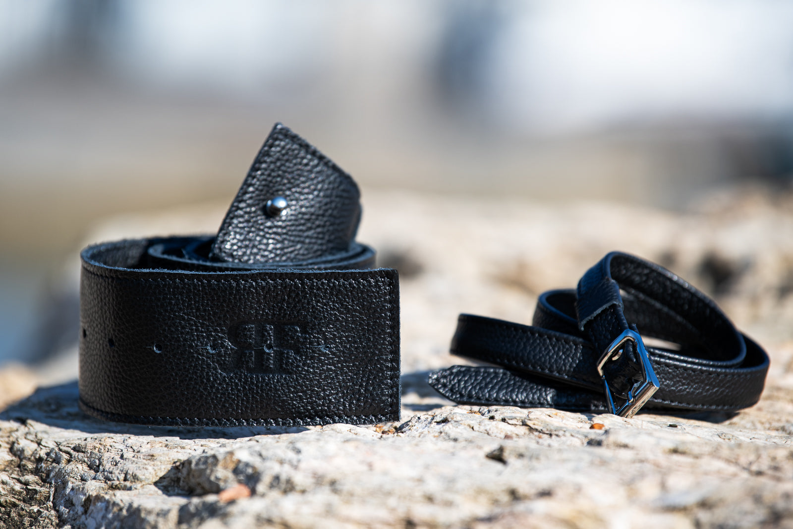 Two black leather belts on a stone surface with a blurred natural background