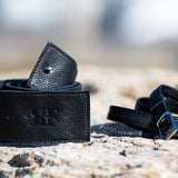 Two black leather belts on a stone surface with a blurred natural background