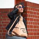 Woman with a beige bag and sunglasses against a brick wall