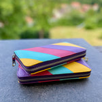 Colorful geometric-patterned wallet on a reflective surface with a blurred natural background