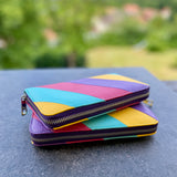 Colorful geometric-patterned wallet on a reflective surface with a blurred natural background