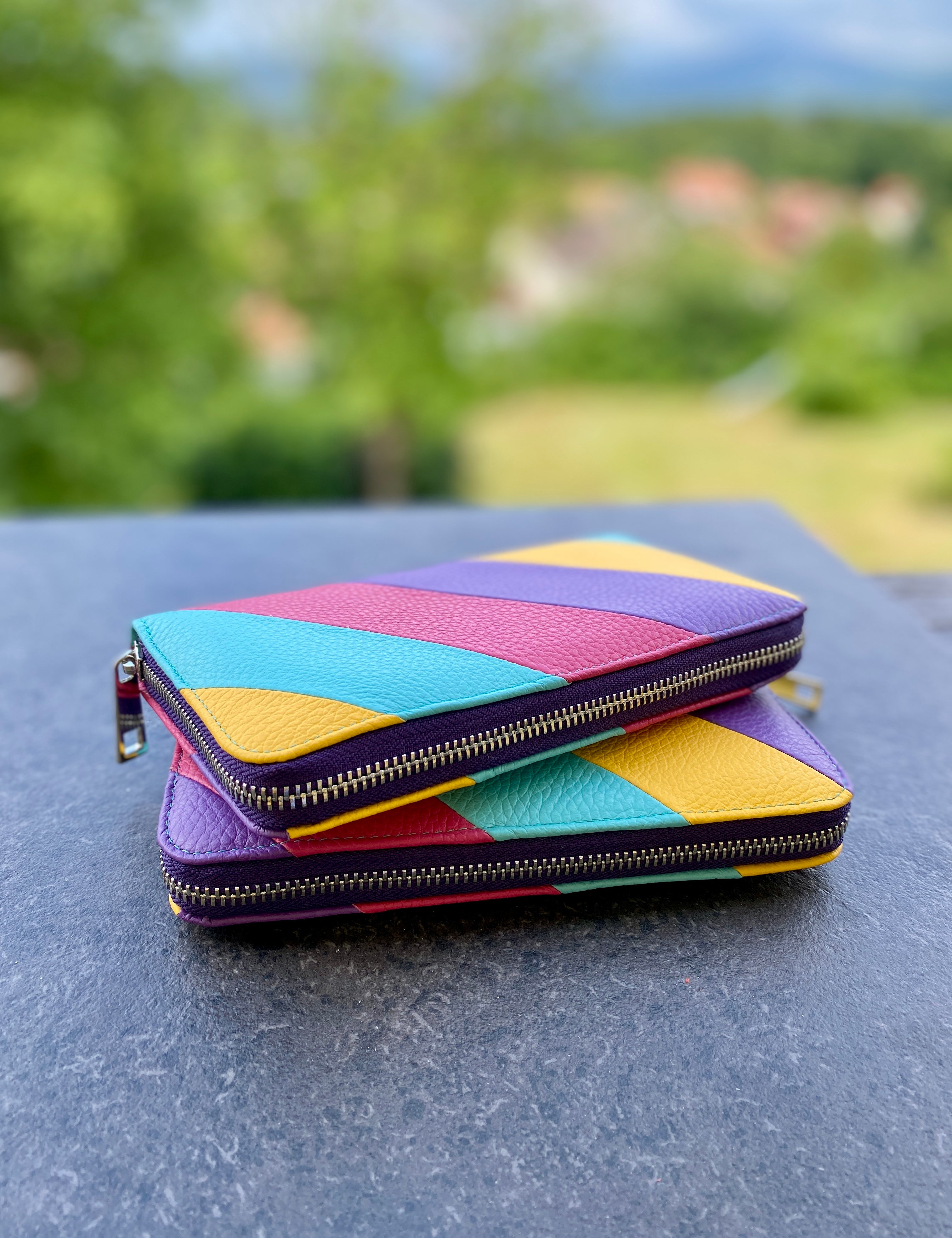 Colorful geometric-patterned wallet on a reflective surface with a blurred natural background