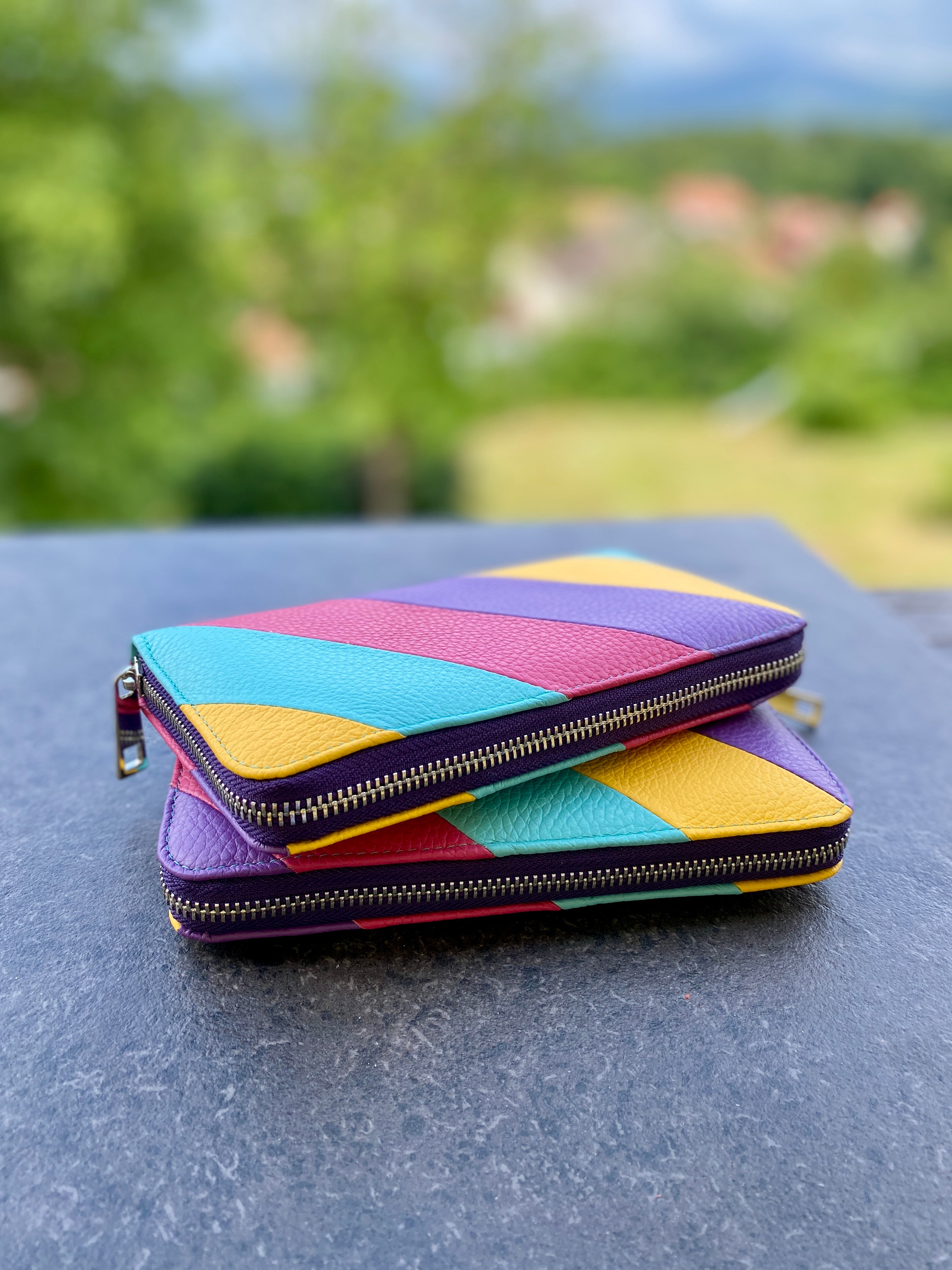 Colorful geometric-patterned wallet on a reflective surface with a blurred natural background