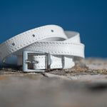 White leather belt with a silver buckle on a textured surface with a blue background