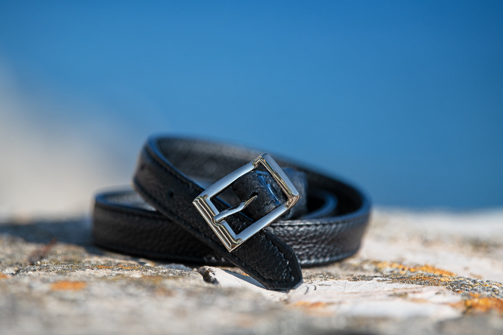 Black leather belt with silver buckle on a textured surface with a blue background