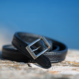 Black leather belt with silver buckle on a textured surface with a blue background