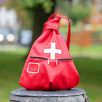 Red backpack with a white cross on a wooden stump in a park setting