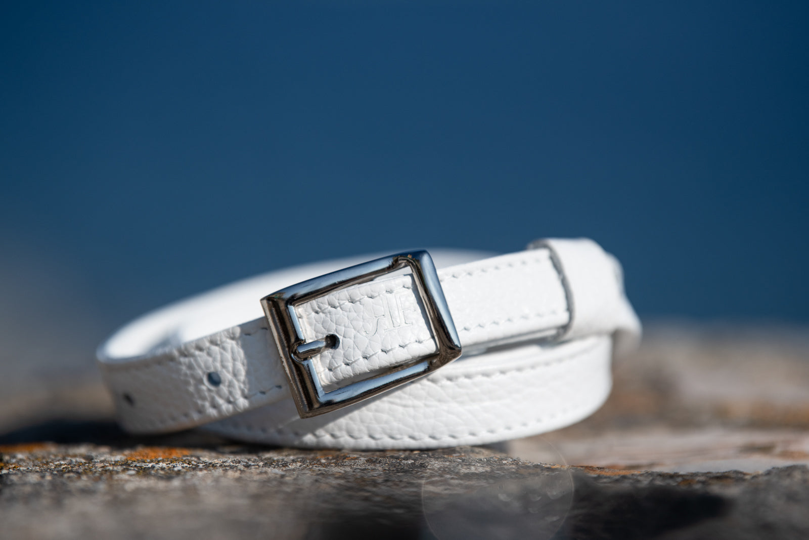 White leather belt with a silver buckle on a stone surface with a blue sky background