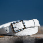 White leather belt with a silver buckle on a stone surface with a blue sky background