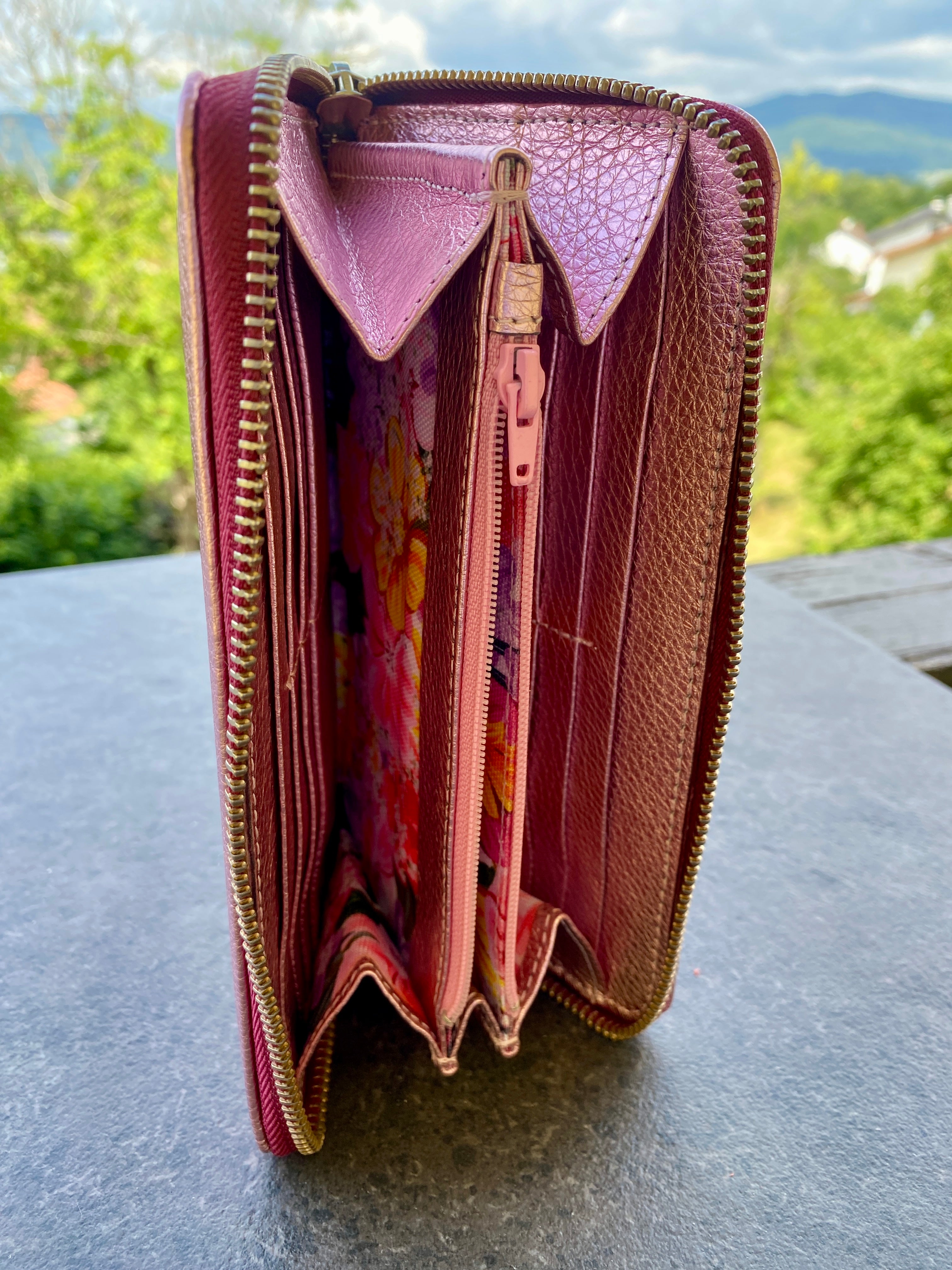 Open pink wallet with floral pattern on a gray surface outdoors