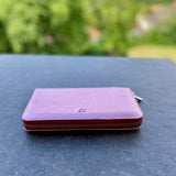 Purple wallet on a dark surface with a blurred green outdoor background