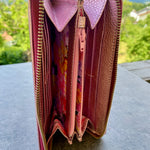 Open pink wallet with floral pattern on a gray surface outdoors