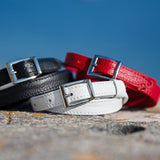 Three dleather belts in black, white, and red on a textured surface with a blue sky background.