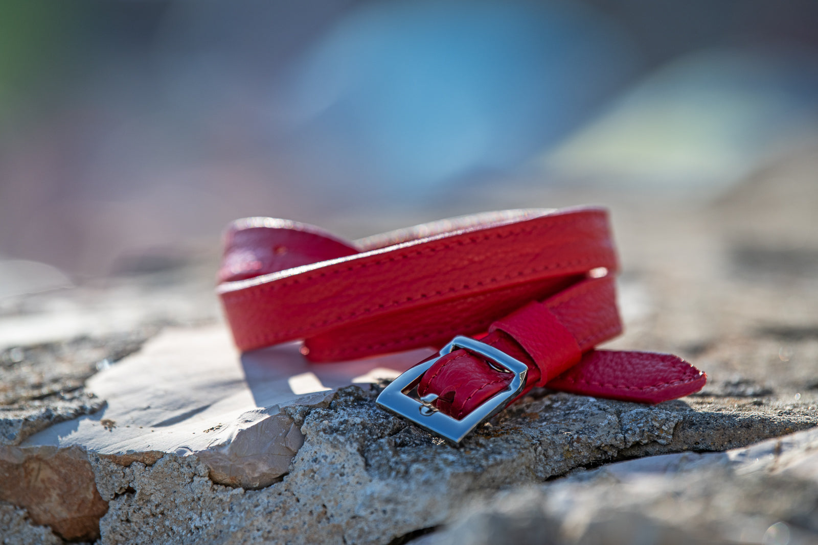 Red belt with a silver buckle on a stone surface with a blurred natural background