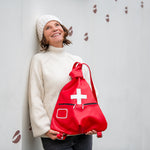Woman holding a red drawstring bag with a white cross against a light gray background