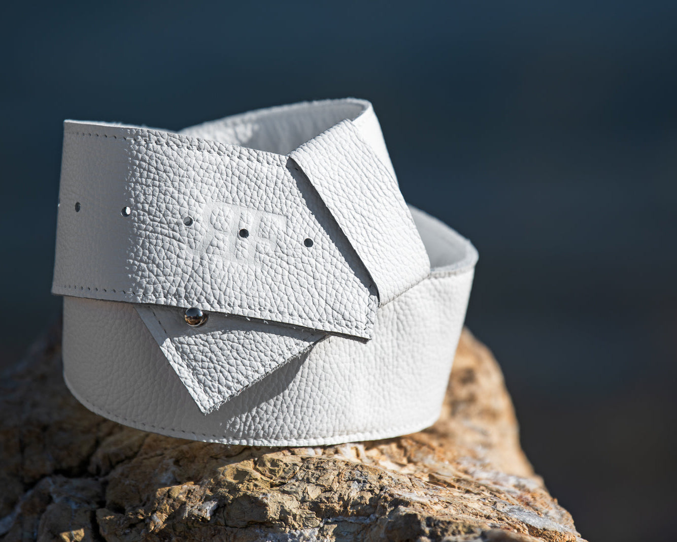 White leather belt on a wooden surface with a blurred natural background