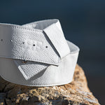 White leather belt on a wooden surface with a blurred natural background