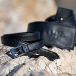 Two black leather belts on a textured stone surface with a blurred natural background.