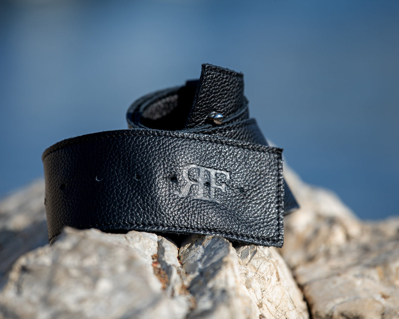 Black leather belt with a logo on a rock against a blurred natural background