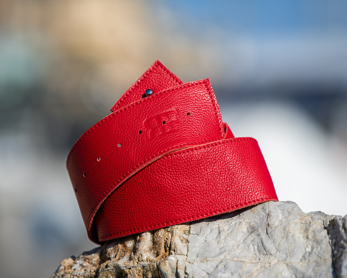 Red leather belt on a wooden surface with a blurred natural background