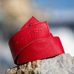 Red leather belt on a wooden surface with a blurred natural background